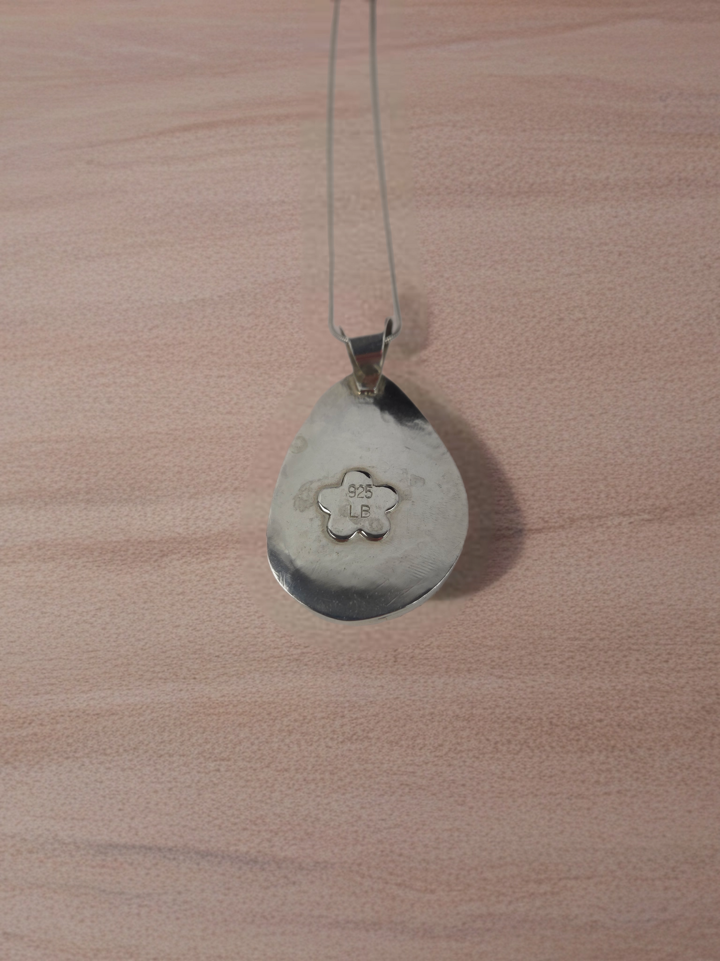 Silver pendant on a chain against a wooden background