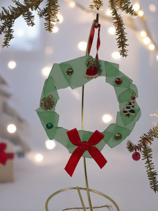 Decorative paper wreath with a red bow and small ornaments on a blurred Christmas tree background.