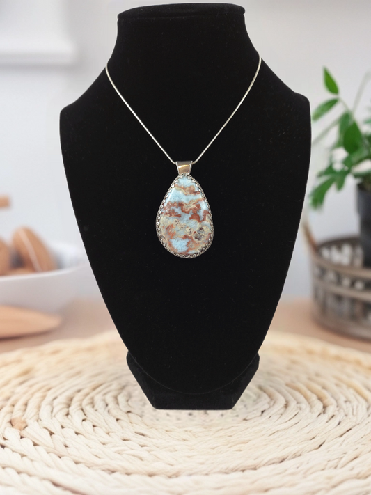 Teardrop-shaped pendant necklace on a black velvet stand with a blurred indoor background