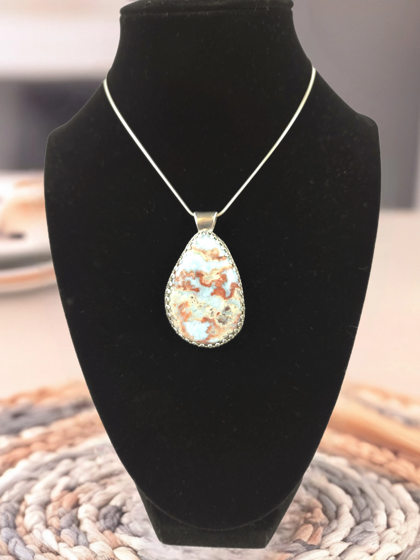 Teardrop-shaped pendant on a black velvet stand with a blurred background