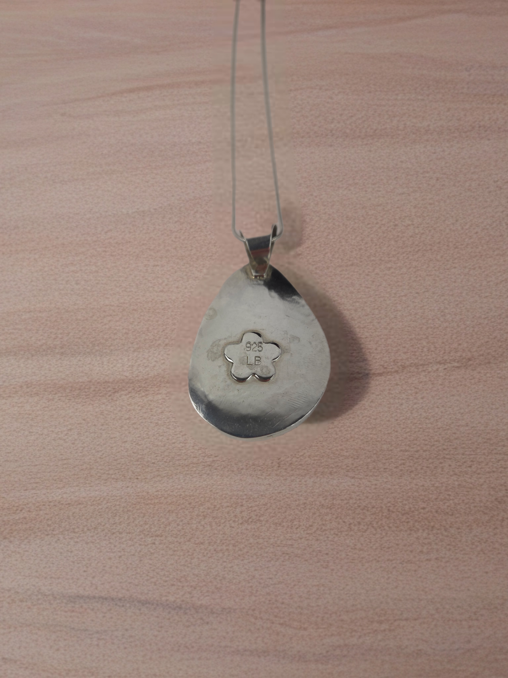 Silver pendant on a chain against a wooden background