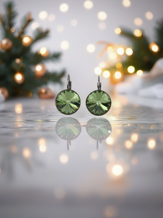 Green gemstone earrings on a reflective surface with blurred Christmas tree and lights in the background