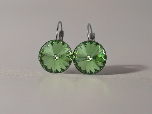 Green gemstone earrings on a reflective surface with a neutral background