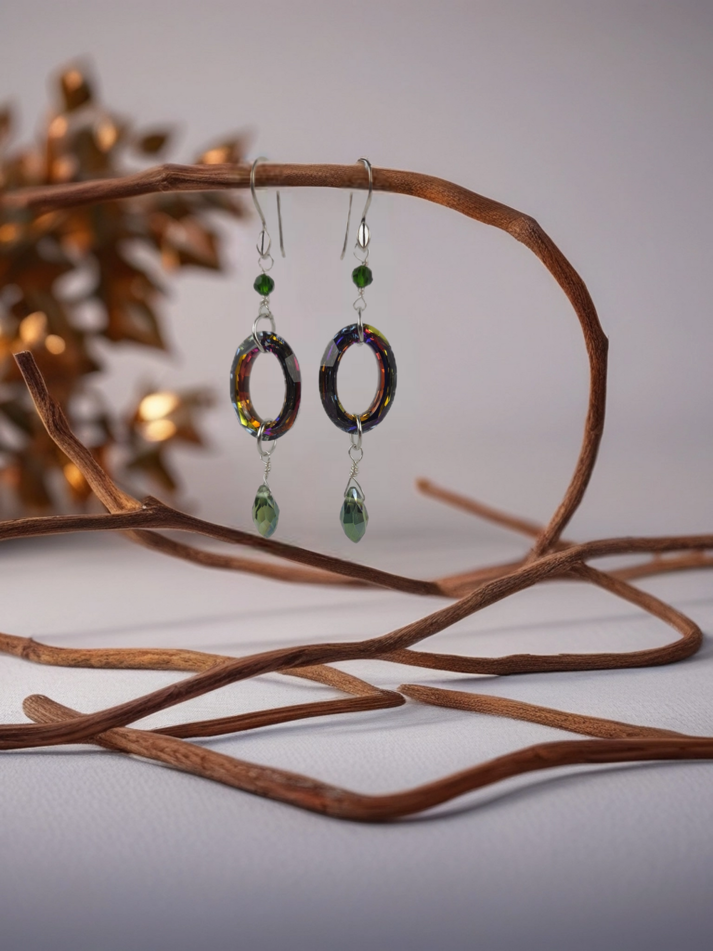 Colorful earrings with green accents hanging on a branch against a blurred background