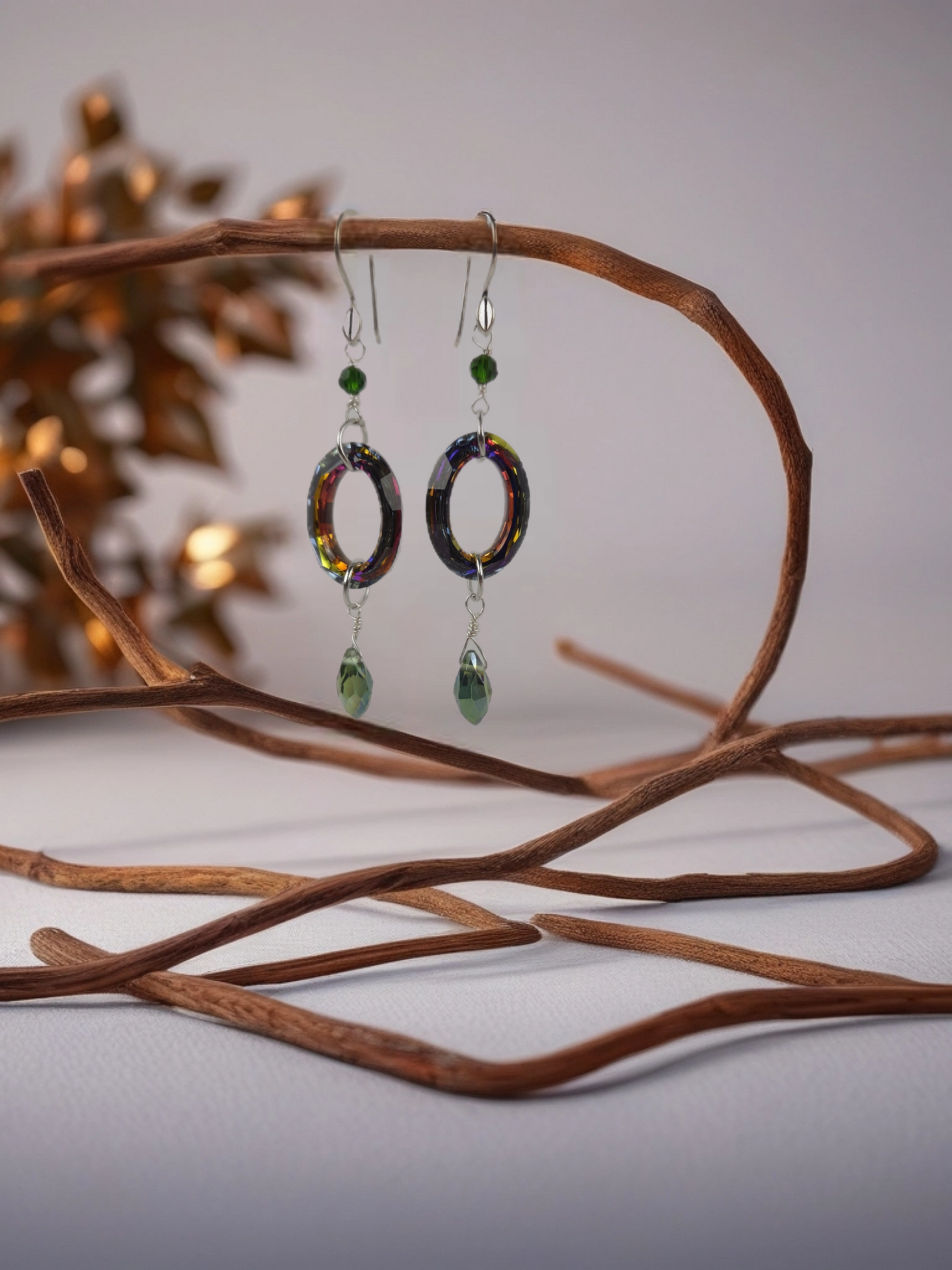 Colorful earrings with green accents hanging on a branch against a blurred background
