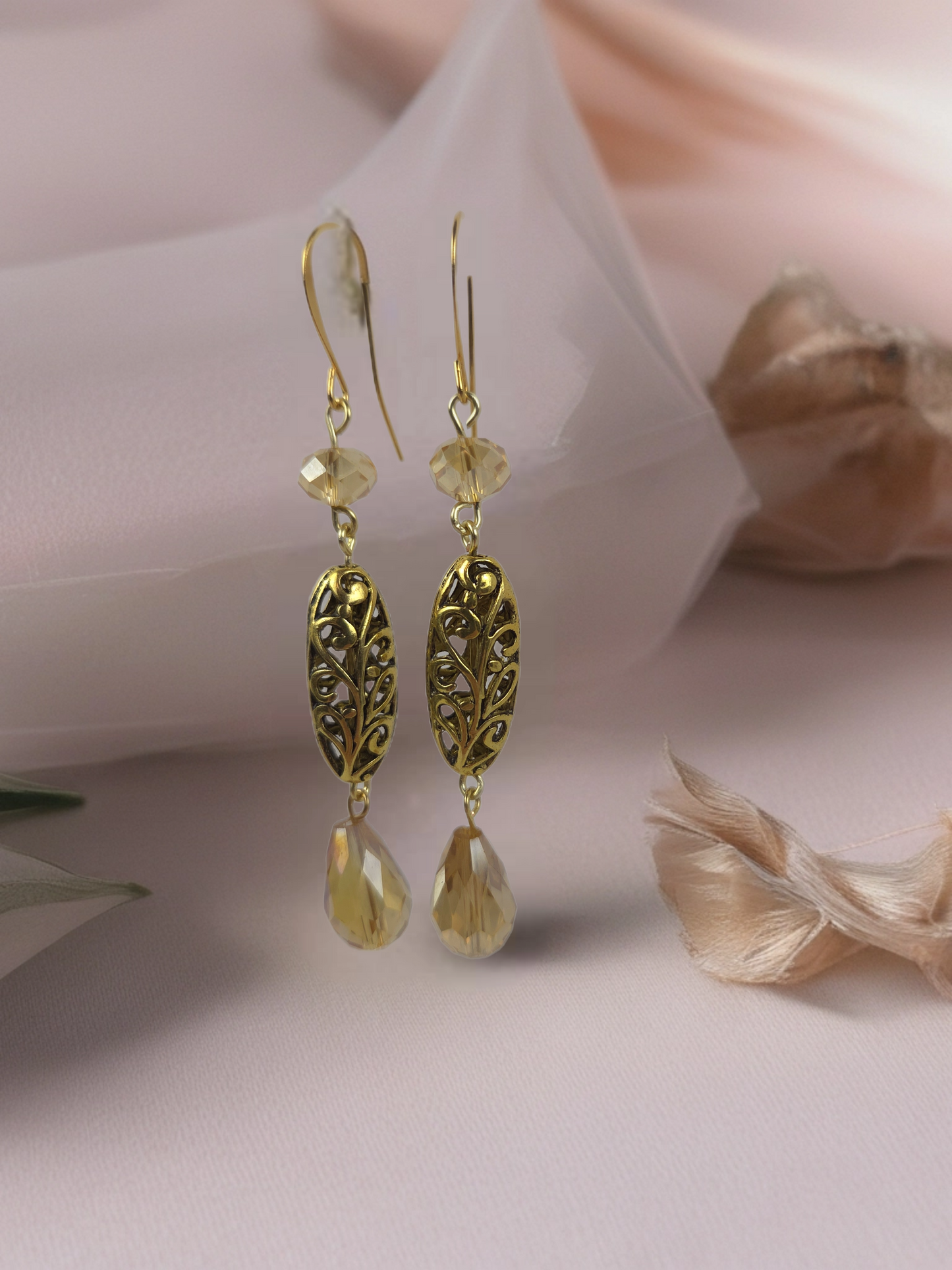 Gold earrings with leaf designs and teardrop shapes on a soft pink background
