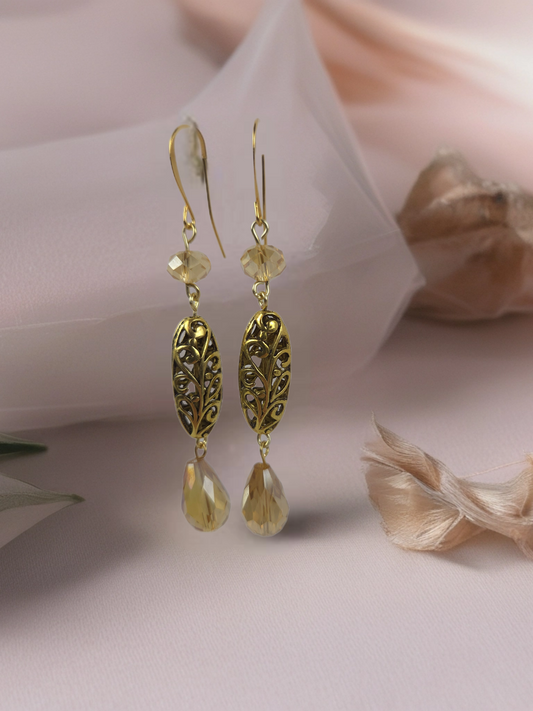 Gold earrings with leaf designs and teardrop shapes on a soft pink background