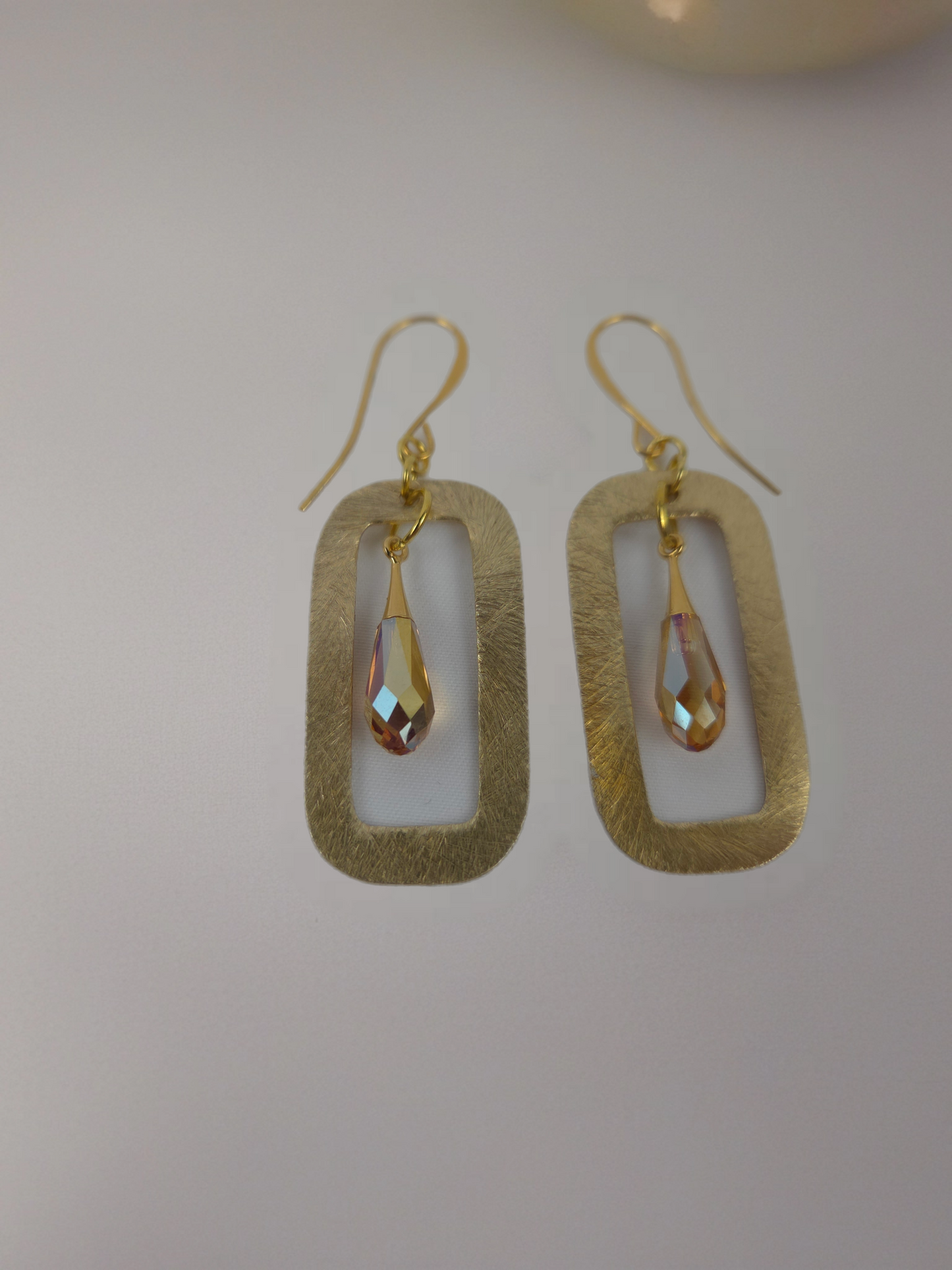 Gold earrings with teardrop-shaped stones on a light gray background