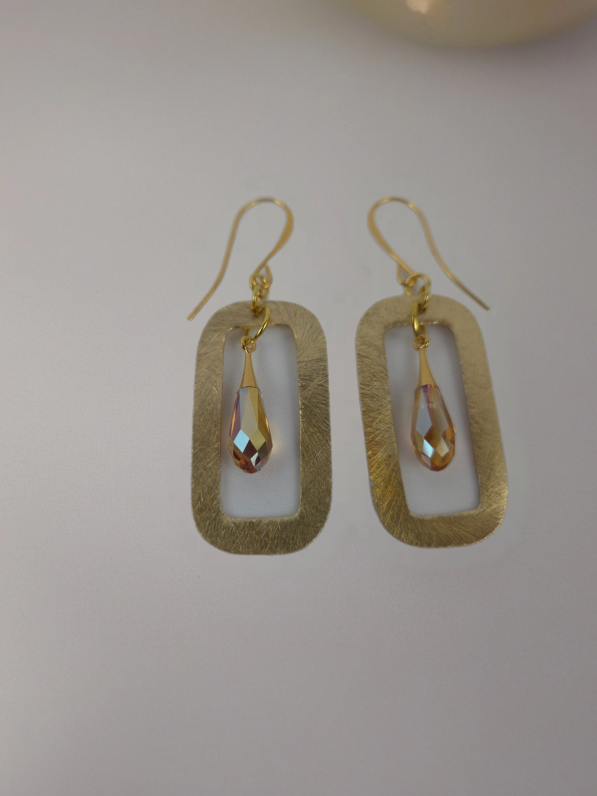 Gold earrings with teardrop-shaped stones on a light gray background