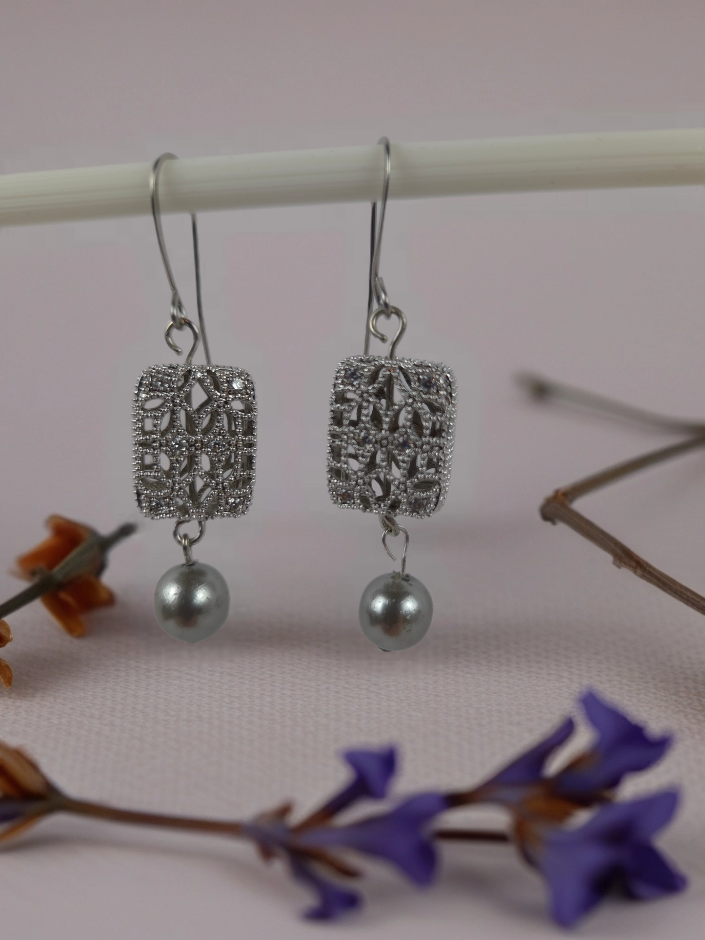 Silver earrings with pearl drops on a pink background with flowers.